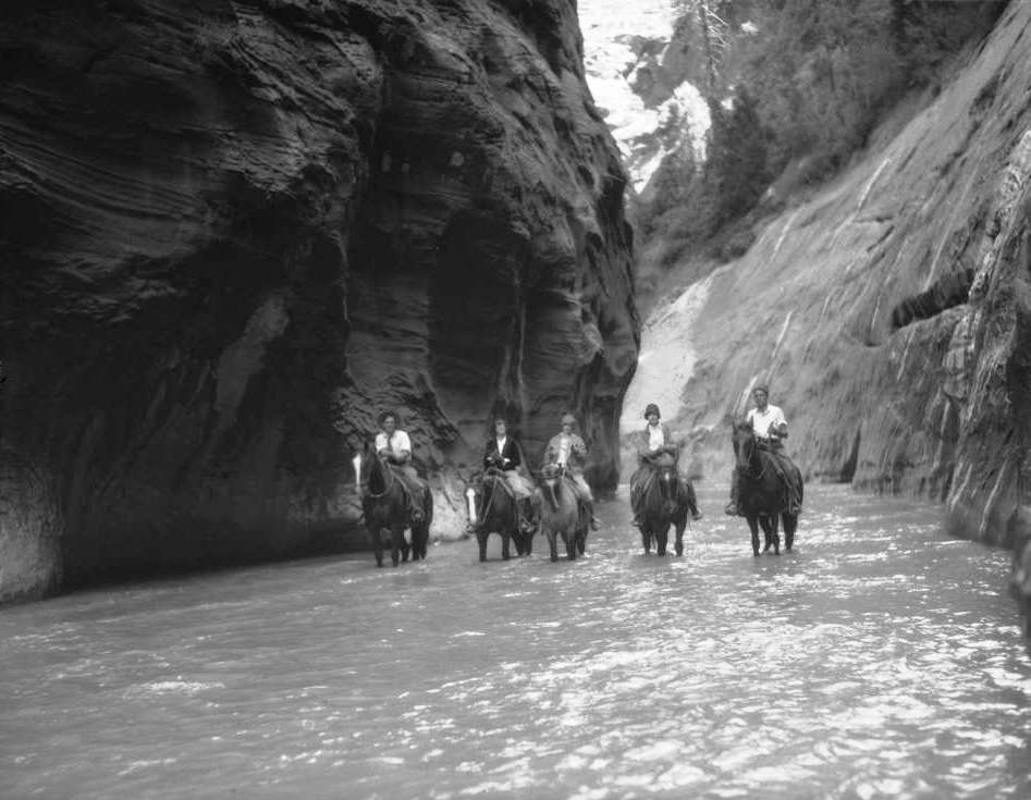 Walter Ruesch, Elsie Baer, Gertrude Grant, Lola Jackson and Vincent Hunter, Union Pacific Railroad photographer, travel on horseback through narrows at Zion National Park, Utah